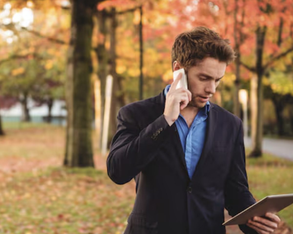 A man in a suit on a phone call in an autumn park, reading from a tablet